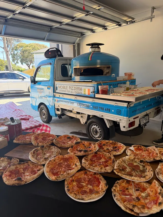 Spread of fresh wood-fired pizzas in front of the blue Antimo Pizza Chef truck