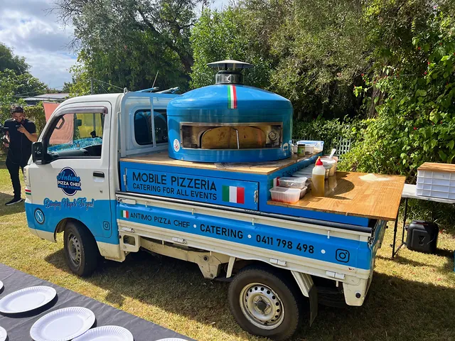The blue Antimo Pizza Chef truck set up on a lawn with its timber serving counter
