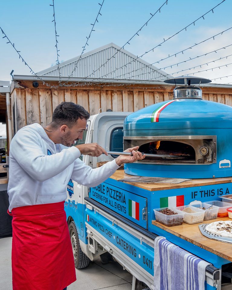 Pizza chef stretching dough at the blue wood-fired oven during a pizza class