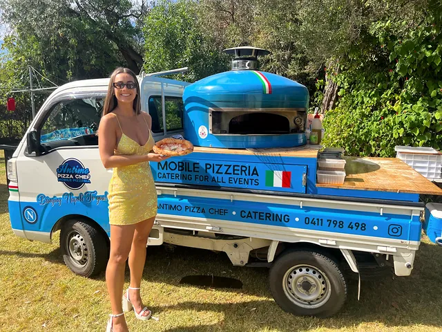 Guest with a fresh pizza next to the blue pizza truck
